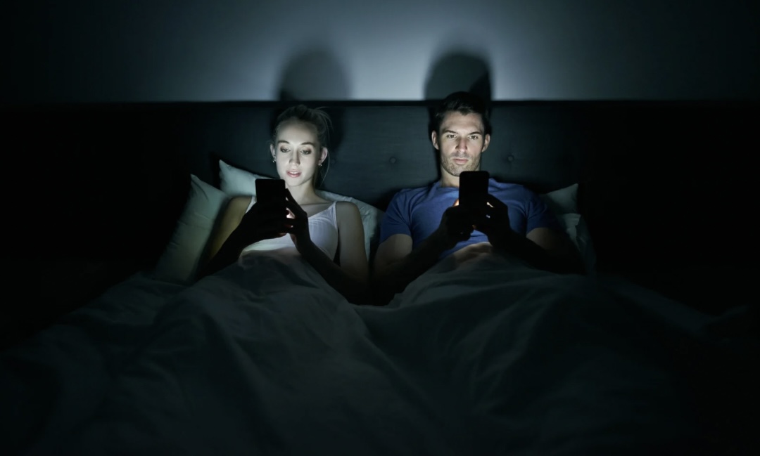Couple sitting together in bed but feeling emotionally distant.