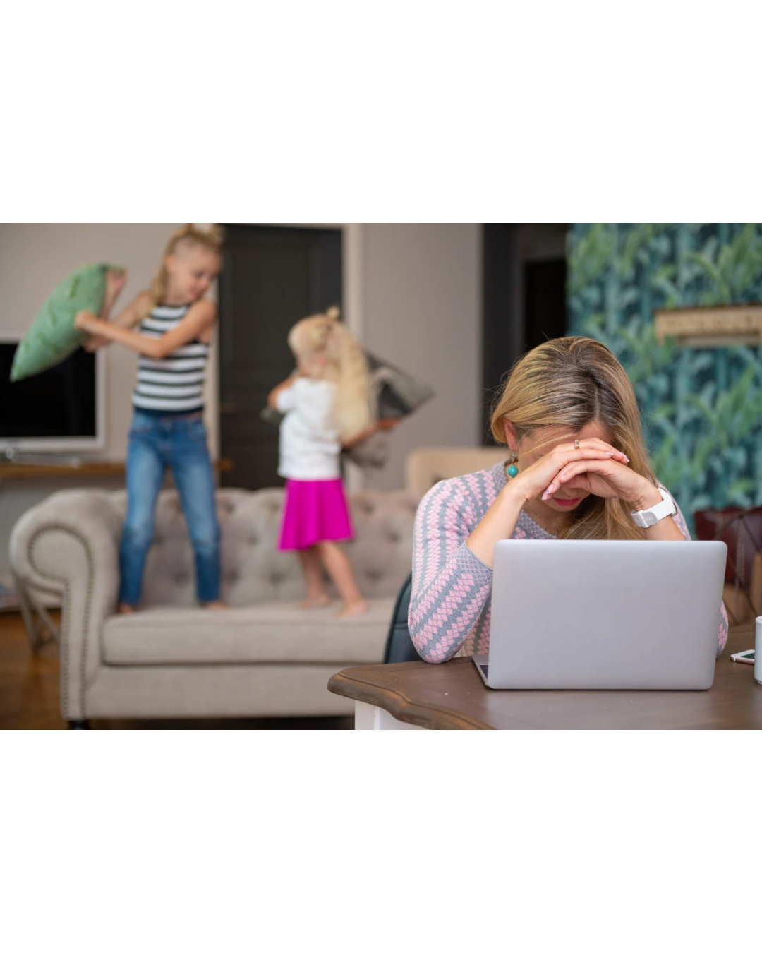 Mother sitting at desk looking overwhelmed while balancing work and parenting responsibilities