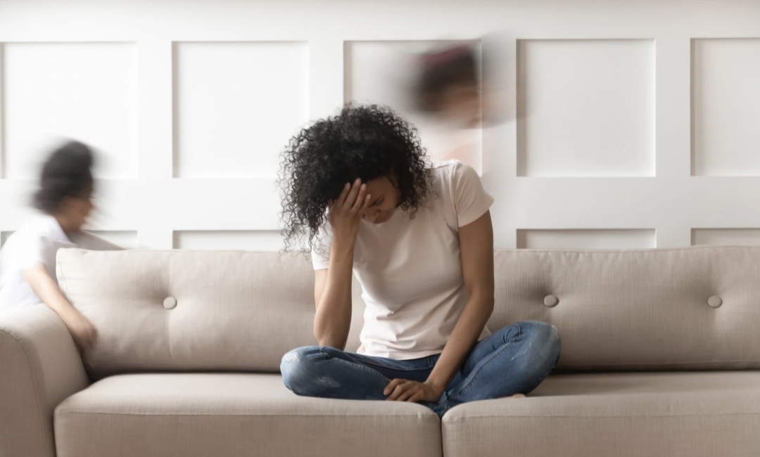 Woman sitting on a couch looking overwhelmed, reflecting on stress and the pressure to regulate her nervous system.